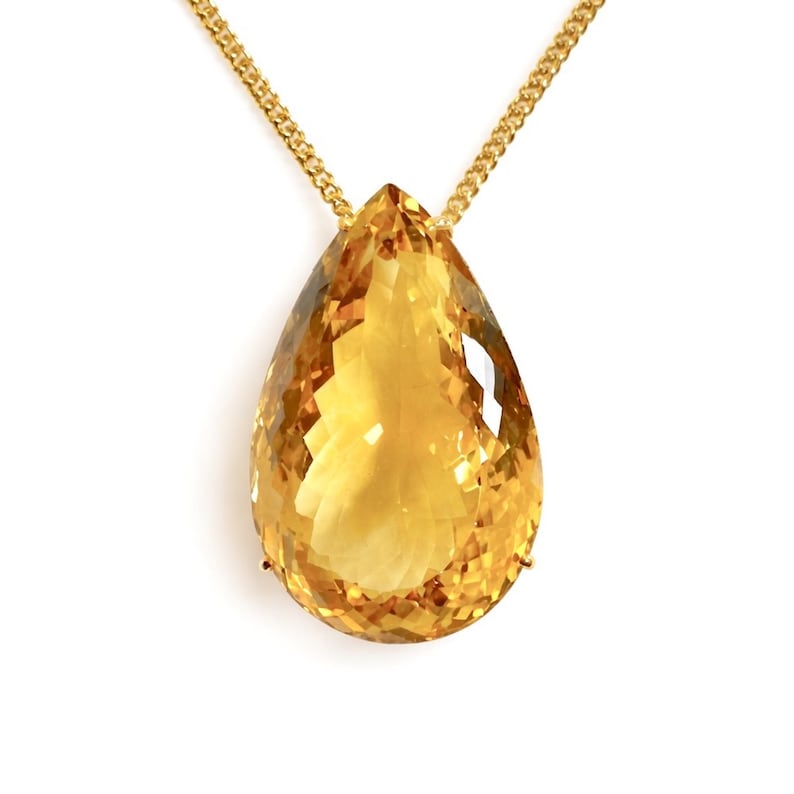 May include: A gold necklace featuring a large, faceted, teardrop-shaped citrine pendant. The pendant is a vibrant yellow-orange color and is suspended from a delicate gold chain. The gemstone is cut to maximize light reflection.