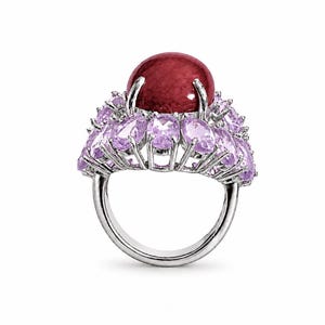 May include: A silver ring featuring a large, round, dark red gemstone at the center, surrounded by a cluster of oval-cut, light purple gemstones. The ring has a polished, metallic band.