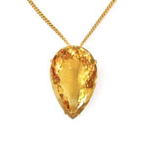 May include: A gold necklace featuring a large, faceted, teardrop-shaped citrine pendant. The citrine is a vibrant yellow-orange color, and the gold chain has a textured, curb link design. The pendant is held in place by small gold prongs.