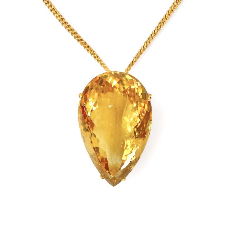 May include: A gold necklace featuring a large, faceted, teardrop-shaped citrine pendant. The citrine is a vibrant yellow-orange color, and the gold chain has a textured, curb link design. The pendant is held in place by small gold prongs.