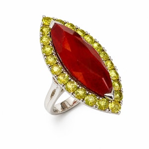 May include: A silver ring featuring a large, marquise-cut, red gemstone center, surrounded by a halo of small, round, yellow-green gemstones. The ring has a polished, metallic band and a bright, white background.