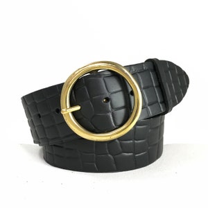May include: Black leather belt with a gold-toned round buckle. The belt has a crocodile-embossed pattern.