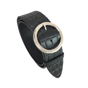 May include: Black belt with a silver-colored, round buckle. The belt has a textured, crocodile-like pattern. The buckle is a large, circular design. The belt is made of a flexible material.