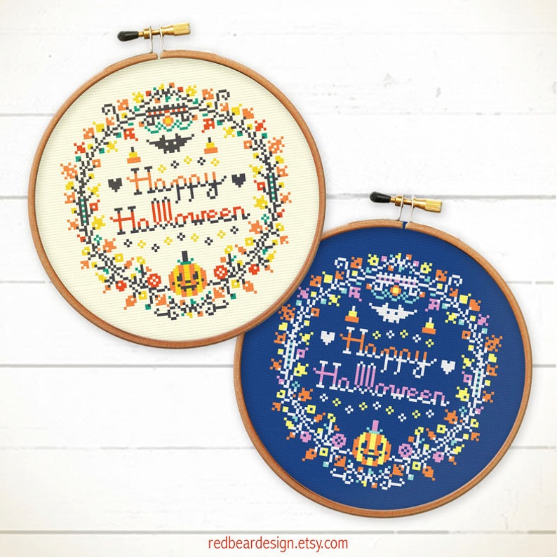 May include: Two cross-stitch hoops with Halloween wreaths. One is on cream fabric, the other on blue. Both feature a pumpkin, bat, and the words "Happy Halloween" in a decorative font. The hoops are set in wooden frames.