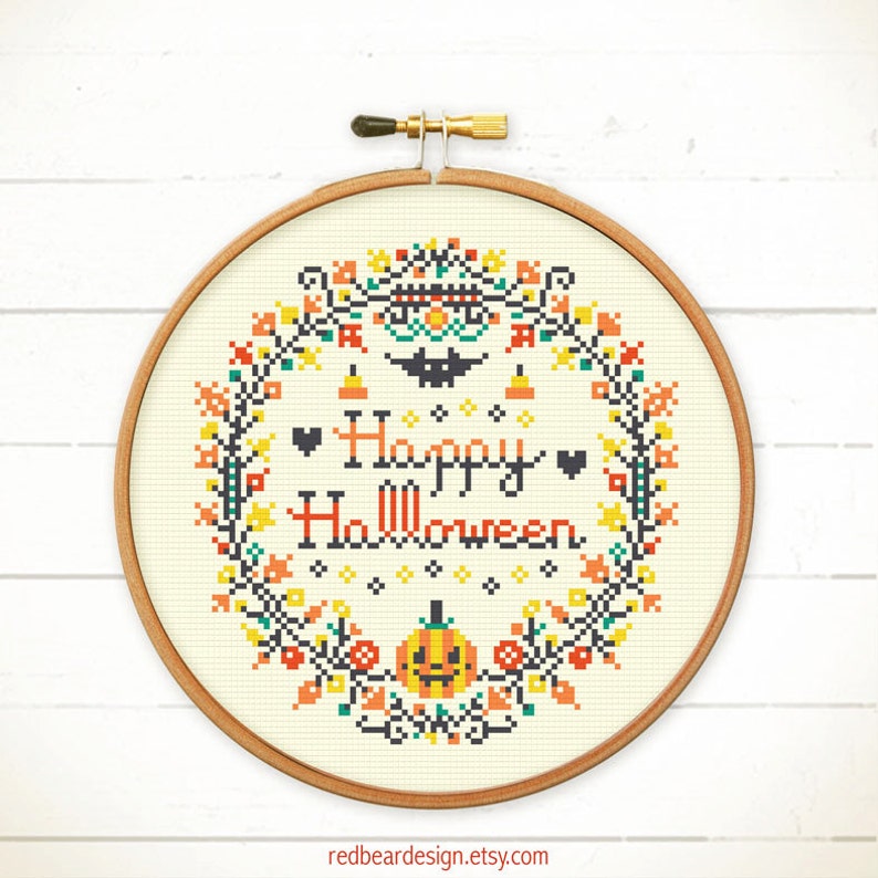 May include: A cross-stitch embroidery hoop with a Halloween theme. The design features the words "Happy Halloween" in black and orange, surrounded by a wreath of colorful autumn leaves, pumpkins, and a bat. The hoop is made of wood.
