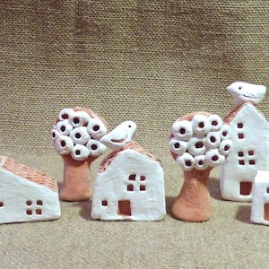 Op de afbeelding: Een set van vijf miniatuur keramische huisjes met witte verf en rode kleiaccenten. Elk huisje heeft een uniek ontwerp, waaronder een vogeltje op het dak, een boom met witte cirkels en een raam met een klein vogeltje-uitsparing.
