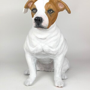 May include: A white and brown dog sculpture sitting with its head tilted to the side. The dog has brown ears and a brown patch on its back.