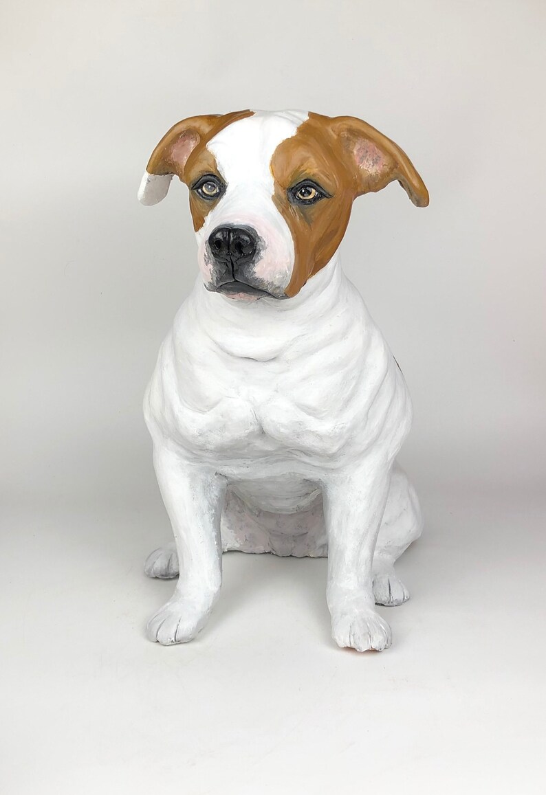 May include: A white and brown dog sculpture sitting with its head tilted to the side. The dog has brown ears and a brown patch on its back.