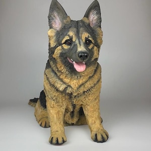 May include: A brown and black German Shepherd dog figurine sitting with its tongue sticking out. The figurine is made of a realistic material and has a detailed face.