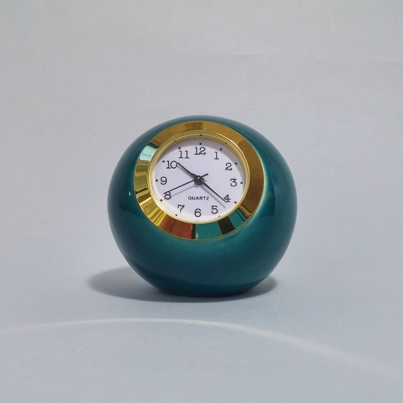 May include: A teal blue round clock with a gold rim and white face. The clock face has black hands and black numbers.