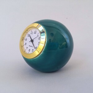 May include: A teal ceramic clock with a gold rim and white face. The clock has black hands and black numbers.