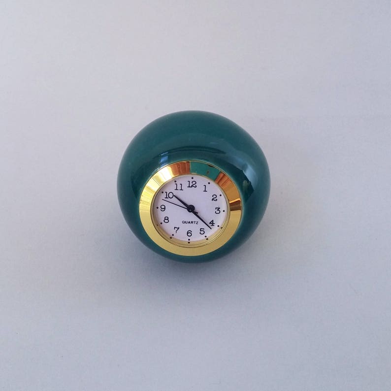 May include: A teal green sphere clock with a gold rim and white face. The clock face has black hands and black numbers.