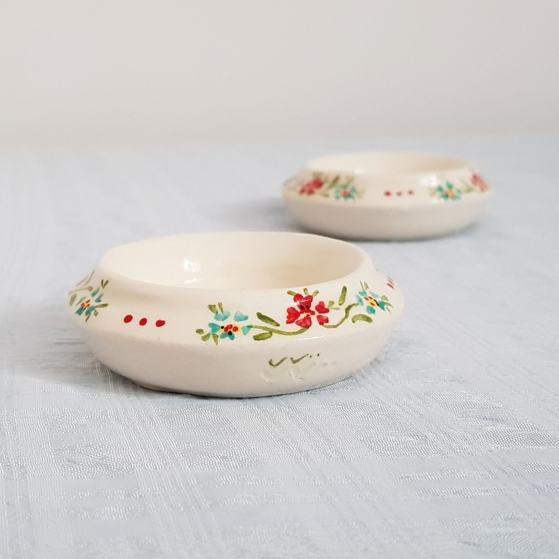 May include: Two small white ceramic bowls with a floral design. The bowls have a green, red, and blue floral pattern around the rim.