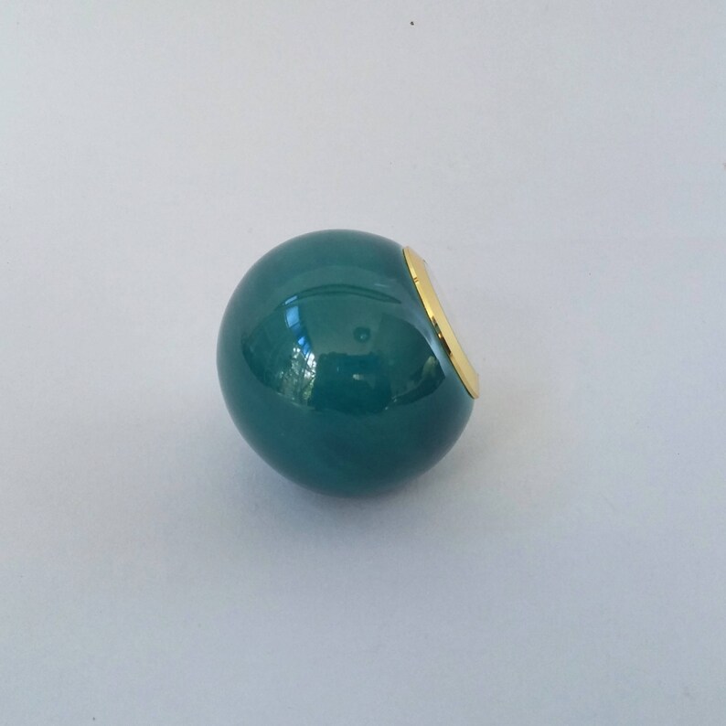 May include: A teal blue sphere with a gold rim. The sphere is smooth and shiny.