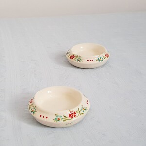 May include: Two small white ceramic bowls with a floral design. The bowls have a raised rim and a floral pattern in red, blue, and green.