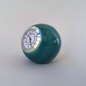 May include: A teal ceramic sphere clock with a silver face and black numbers. The clock reads "QUARTZ" and has a silver rim.