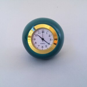 May include: A green round clock with a gold rim and white face. The clock has black hands and black numbers.