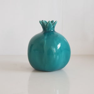May include: A teal ceramic pomegranate vase with a detailed, textured top.
