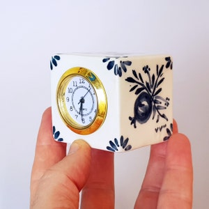 May include: A white ceramic clock with a gold rim around the face. The clock has black and blue floral designs and the words "Quartz" and "Swiss" on the face.