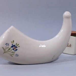 May include: White ceramic salt cellar shaped like a horn with blue and green floral designs. The cellar is sitting next to a small white ceramic container with the word "Salt" written on it.