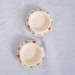 May include: Two small white ceramic bowls with a floral design. The bowls have a red, blue, and green floral pattern around the rim.