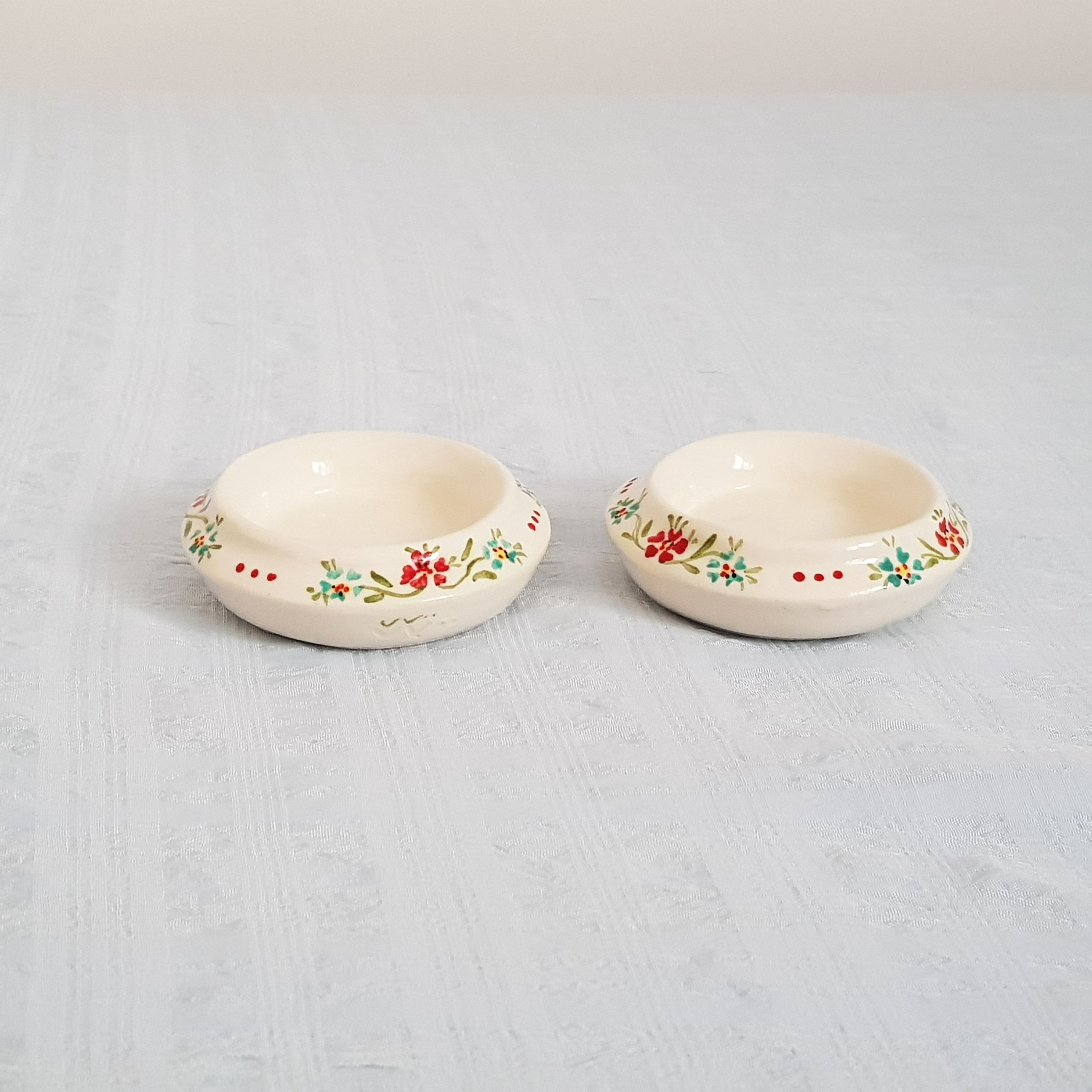 May include: Two small white ceramic bowls with a floral design. The bowls have a red, green, and blue floral pattern around the rim.