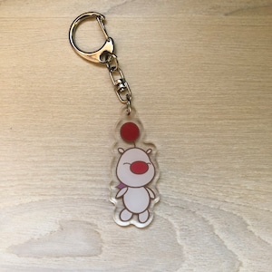 May include: A white and red cartoon character keyring with a red balloon. The character has a small red nose and a big smile. The keyring is made of clear acrylic.