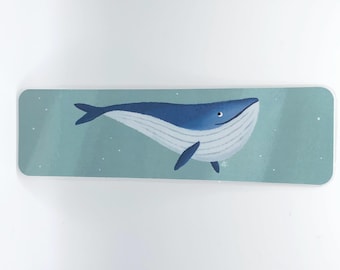 May include: A rectangular bookmark with a blue whale illustration. The whale is in shades of blue and white, set against a light teal background with small white dots. The bookmark has rounded corners.