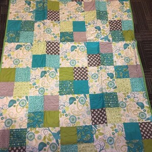 Pode incluir: Um edredom artesanal com um design de patchwork. O edredom apresenta quadrados em tons de verde-azulado, verde, castanho e branco. Alguns quadrados t&ecirc;m padr&otilde;es florais e paisley, enquanto outros t&ecirc;m bolinhas. O edredom &eacute; adornado com uma borda verde.