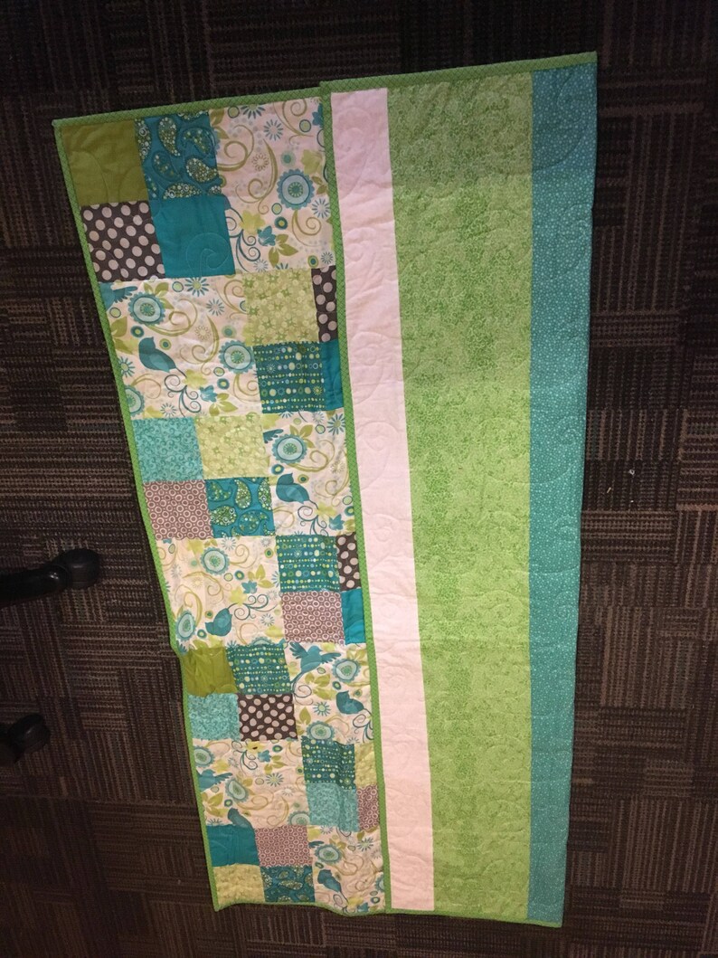 Pode incluir: Um edredom feito &agrave; m&atilde;o com um design de patchwork com quadrados de tecidos turquesa, verdes e castanhos. O edredom tem uma faixa branca no centro e uma borda verde lisa. O edredom tem aproximadamente 152 cm de comprimento.