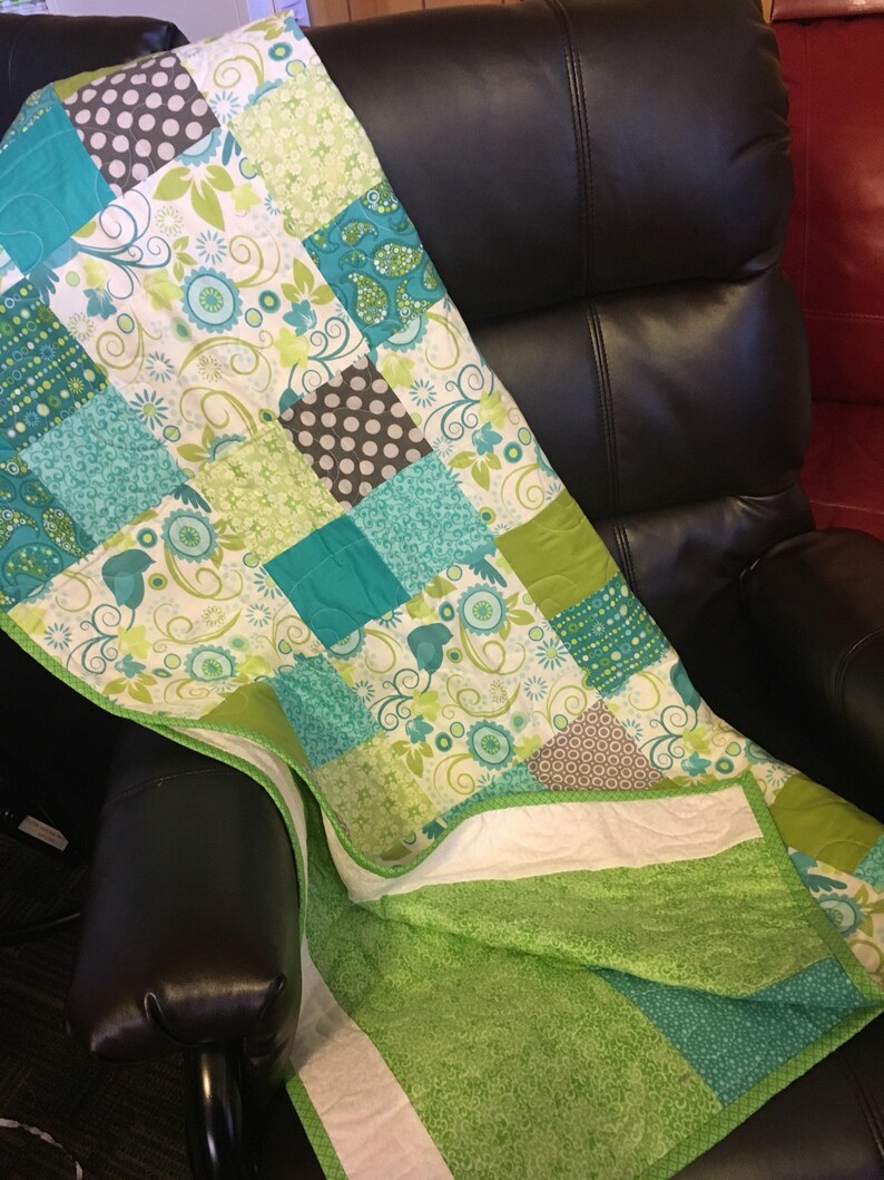 Pode incluir: Um edredom de retalhos com uma variedade de padr&otilde;es e cores, incluindo turquesa, verde, branco e castanho. O edredom apresenta desenhos florais e de bolinhas, com uma borda verde e um verso branco. O edredom est&aacute; sobre uma cadeira preta.