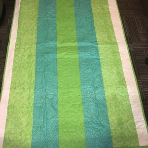 Pode incluir: Um edredom feito &agrave; m&atilde;o com um padr&atilde;o listrado em tons de verde e verde-azulado. O edredom apresenta um painel central verde brilhante, ladeado por listras verde-azulado com bolinhas brancas. Bordas brancas emolduram as bordas.
