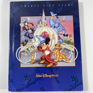 May include: A blue book cover with a white carriage and various Disney characters, including Mickey Mouse, Goofy, and Genie. The text on the cover reads "Walt Disney World Twenty-Five Years".
