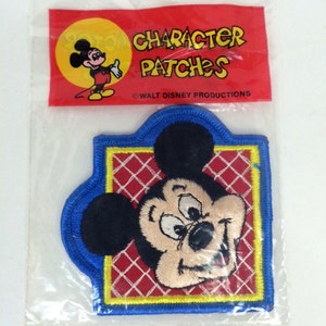 May include: A vintage Mickey Mouse character patch in a plastic bag. The patch is red, yellow, and blue with a white grid pattern. The patch features a close-up of Mickey Mouse's face. The bag has a red label that reads "Character Patches" and "Walt Disney Productions".