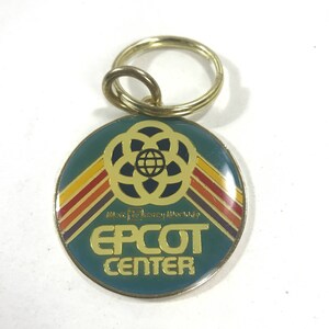May include: A gold-colored metal keychain with a green, yellow, orange, and red striped design. The keychain features the Walt Disney World logo and the text "EPCOT CENTER".