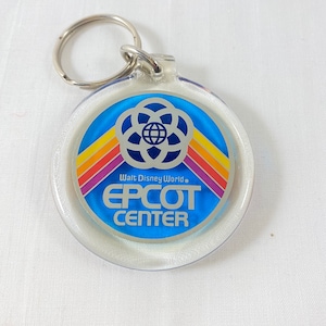 May include: A clear plastic keychain with a blue circle featuring the Epcot Center logo. The logo includes a globe with a stylized flower design and the text "Walt Disney World." and "EPCOT CENTER".