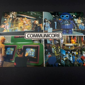 May include: A vintage postcard featuring a photo montage of the CommuniCore, a futuristic interactive exhibit. The postcard shows a blue robot, a large screen with a game, and a variety of people interacting with the exhibits.