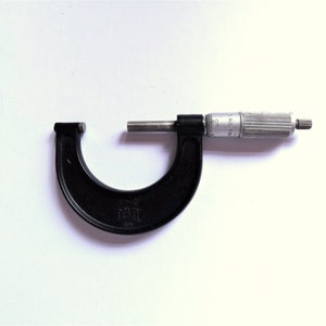 May include: A black micrometer with a silver spindle and a knurled grip. The micrometer has a C-shaped frame and is marked with measurements. The tool is used for precise measurements of small objects, with a measurement range of 2.5-5.1 cm.