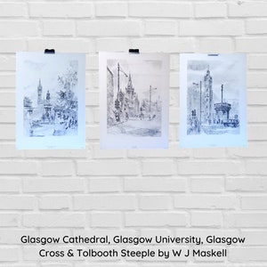 May include: Three framed black and white prints of Glasgow landmarks, including Glasgow Cathedral and Glasgow University, are displayed against a white brick wall. The prints are held by black clips. The text at the bottom reads: Glasgow Cathedral, Glasgow University, Glasgow Cross & Tolbooth Steeple by W J Maskell.