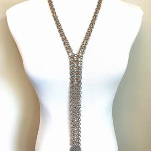 Puede incluir: Un collar largo de cadena de plata y cobre con un borla en la parte inferior. El collar está en capas y tiene un diseño en forma de V.
