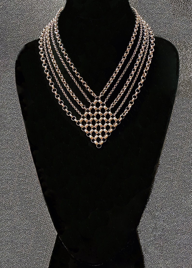 Op de afbeelding: Een zilveren meerrijige ketting met een geometrisch ontwerp. De ketting is gemaakt van meerdere kettingen met kleine, ronde kralen.