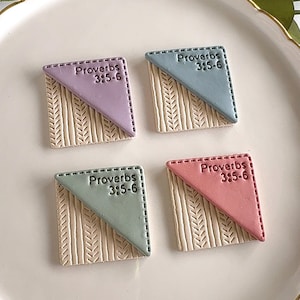 May include: Four square, decorative tiles with the text "Proverbs 3:5-6". Each tile has a different color: lavender, blue, green, and pink. The bottom portion of each tile has a wheat stalk design.