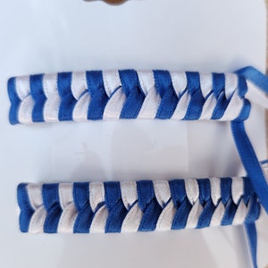 May include: Two blue and white braided ribbon hair ties. The ribbons are woven together in a criss-cross pattern.
