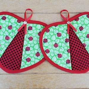 May include: Two red and green heart-shaped pot holders with a ladybug pattern. The pot holders have a red polka dot fabric in the center.