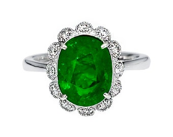 May include: A silver ring featuring a large oval emerald gemstone set within a halo of smaller diamonds.