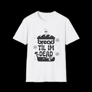 May include: White t-shirt with a black graphic that reads "bread til im dead". The design includes a loaf of bread, mushrooms, flowers, and a skull. A casual, fun tee for everyday wear.