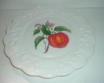 May include: White milk glass plate with a raised floral design around the edge. The center of the plate features a painted image of a red apple with green leaves and pink flowers.