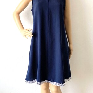 May include: A navy blue sleeveless dress with white lace trim around the neckline and hem. The dress is knee-length and has a simple, A-line silhouette.