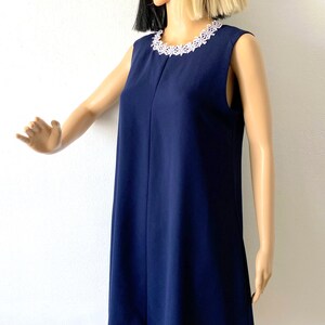 May include: A sleeveless navy blue dress with a white lace trim around the neckline and hem. The dress is fitted at the top and flows out to a slightly flared hem.