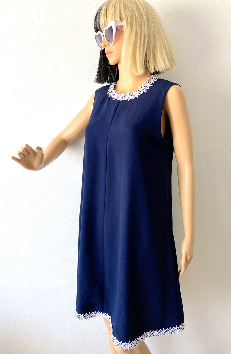 May include: A sleeveless navy blue dress with a white lace trim around the neckline and hem. The dress is fitted at the top and flows out to a slightly flared hem.